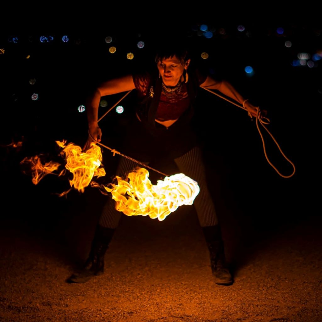 Performer spinning FIRE MECCA fire rope dart in motion, flames trailing dramatically to emphasize flow and visual impact.