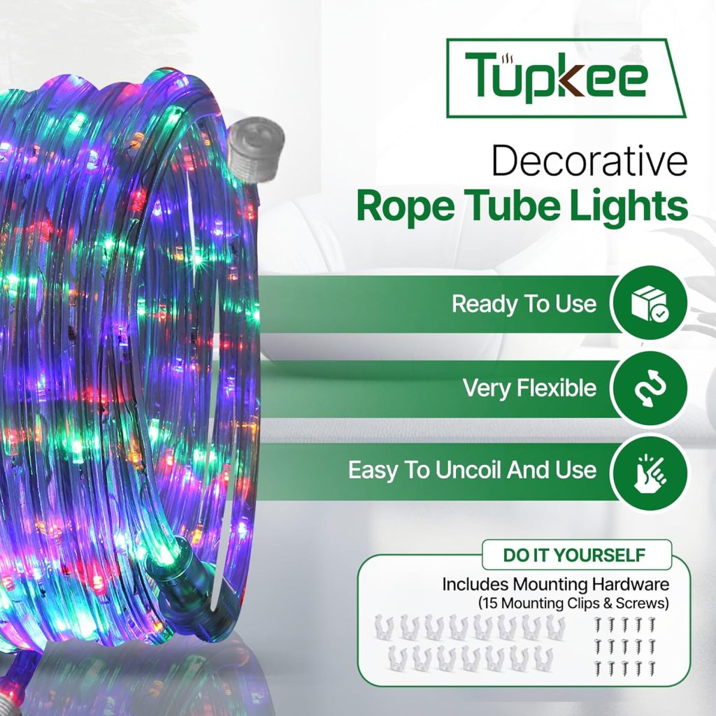 A low-angle shot of a multi-colored LED rope light from Tupkee, illuminating a dark room. The light is draped over a bed's headboard, casting vibrant red, blue, and green hues onto the surrounding walls and furniture.
