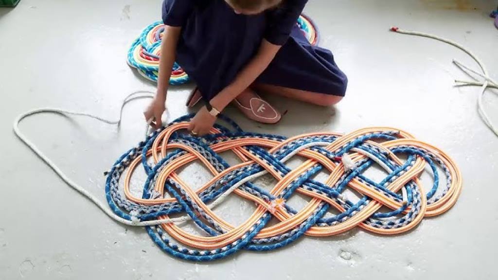 A vibrant, multicolored nautical rope rug with navy and coral hues, displayed on a porch