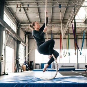Aerial rope artist climbing a vertical rope in a bright training studio