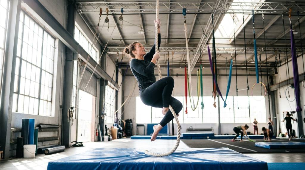 Aerial rope artist climbing a vertical rope in a bright training studio